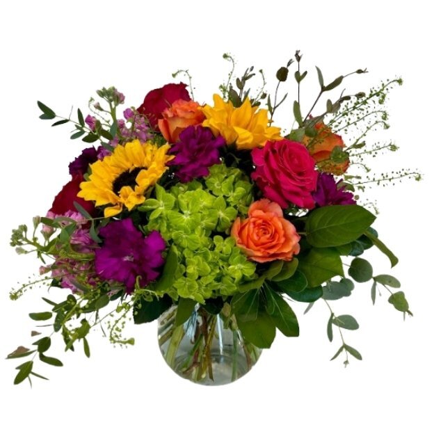 Bright mixed floral arrangement featuring sunflowers, roses, hydrangea, and colorful accent flowers in a round glass vase.